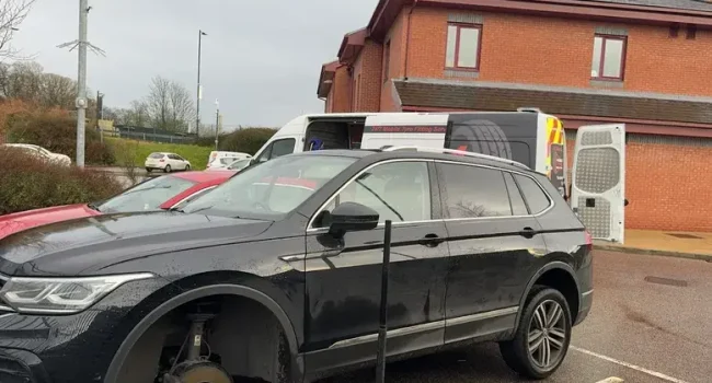Mobile tyre fitter changing tyre on black VW SUV at customer's home